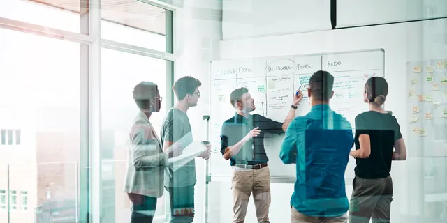 Five colleagues planning work together at an office whiteboard